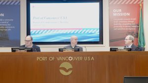 Three men sit behind a large desk. A screen behind them reads Port of Vancouver Board of Commissioners Meeting